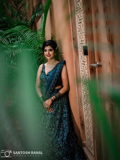 We play with composition to create visually interesting shots. Here, the use of foreground foliage frames the model in her sparkling blue reception lehenga, adding depth and drawing the viewer's eye to her confident pose.