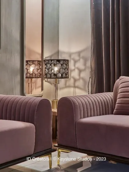 A detail of the plush, channel-tufted sofa in a dusty rose velvet, complemented by a modern table lamp with a hexagonal shade.