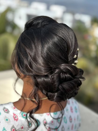 A soft and romantic low bun with intricate weaving, decorated with small gold beads.