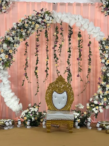 This elegant circular arch with peach and purple floral arrangements serves as a beautiful backdrop for a half-saree function. The ornate golden chair adds a touch of royalty to the setup.