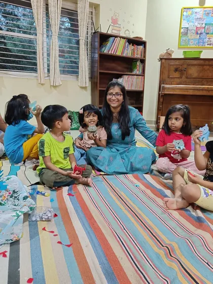 A storyteller sits with the children on the floor, helping them with their paper bear craft.