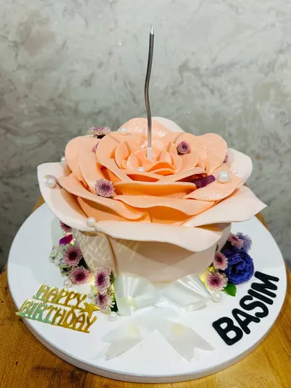 A stunning cake sculpted into a blooming peach-colored rose, with a single candle in the center.