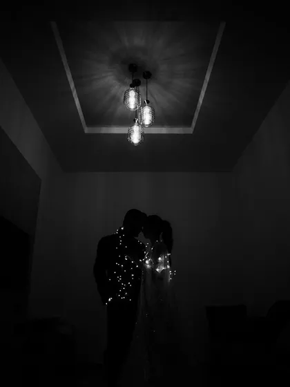 A romantic silhouette of the couple wrapped in fairy lights, their forms barely visible in the dark, creating an intimate and magical atmosphere.