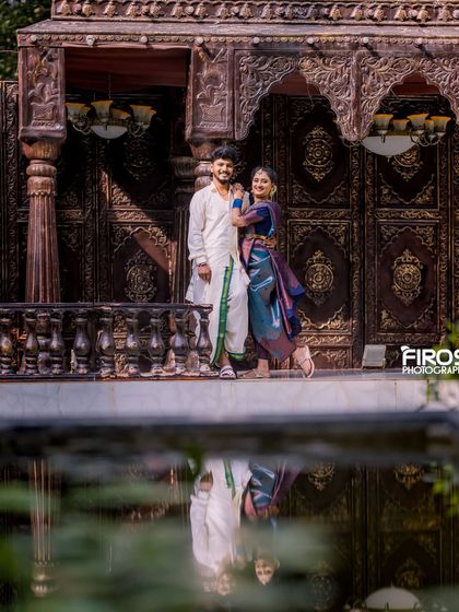 A beautiful reflection shot of the couple in traditional attire by the water, with ornate doors in the background.