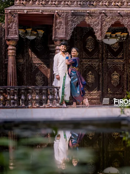 A beautiful reflection shot of the couple in traditional attire by the water, with ornate doors in the background.