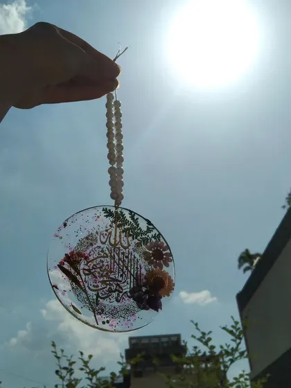 Holding the Ayatul Kursi car hanging up to the sun, showing its beautiful transparency and the embedded elements.