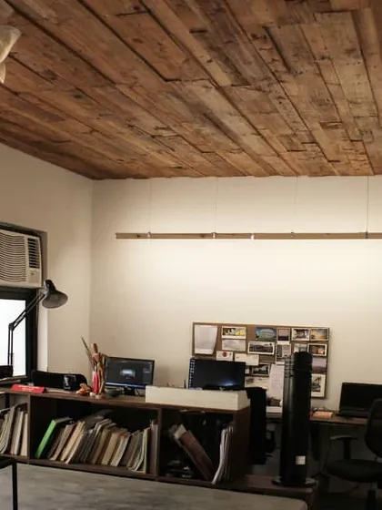 The interior of one of our earlier studios, featuring a ceiling made from recycled wood planks. The design emphasizes natural materials, custom lighting, and an efficient, layered workspace.