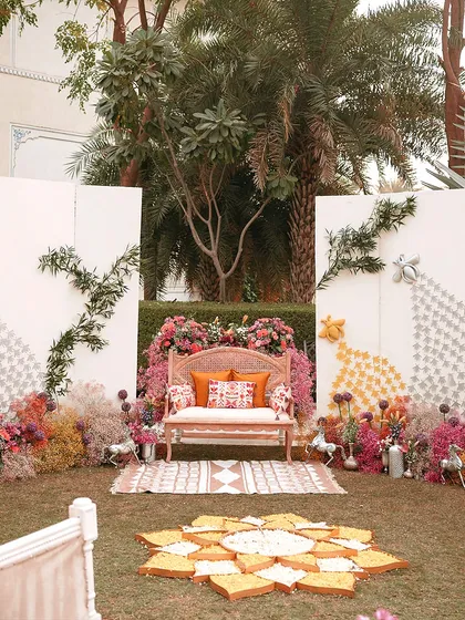 A wide shot of the 'Hall of Flowers' Haldi setup. The lush green lawn is contrasted with bursts of pink, orange, and yellow, creating a stunning visual spectacle.