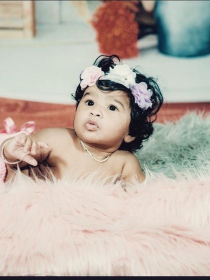A sweet baby girl with a floral headband, captured during a tummy time pose on a soft pink fur rug.