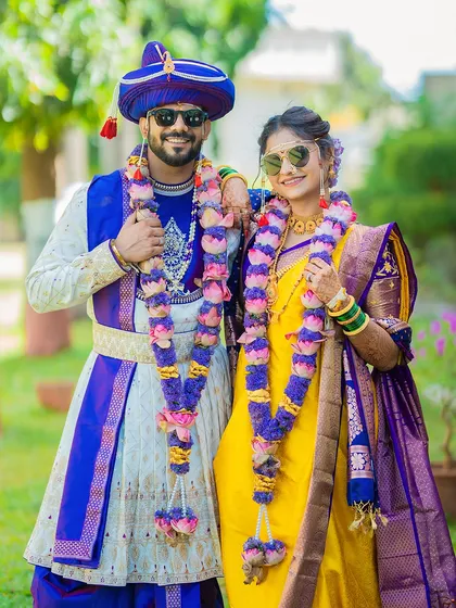 A fun and stylish portrait of a couple in their coordinated blue and yellow wedding outfits, complete with sunglasses for a modern twist.