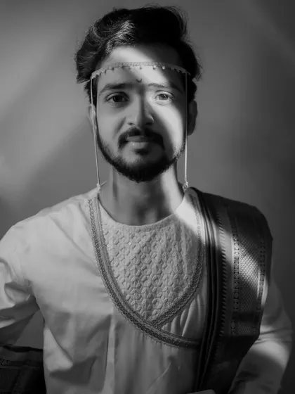 A striking black and white portrait of a groom, with dramatic lighting creating shadows across his face, highlighting the traditional 'mundavalya'.