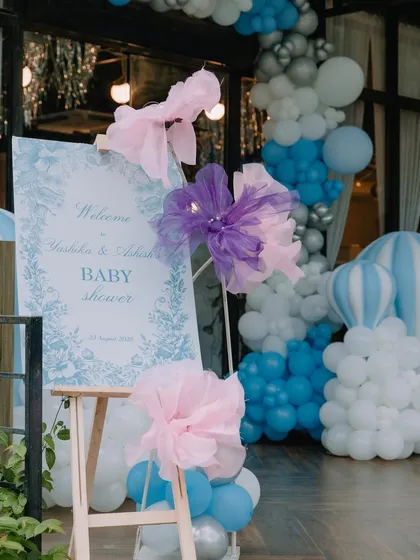 The welcome sign for a blue-themed baby shower, adorned with large, artistic paper flowers and set against a backdrop of a blue, white, and silver balloon arch.