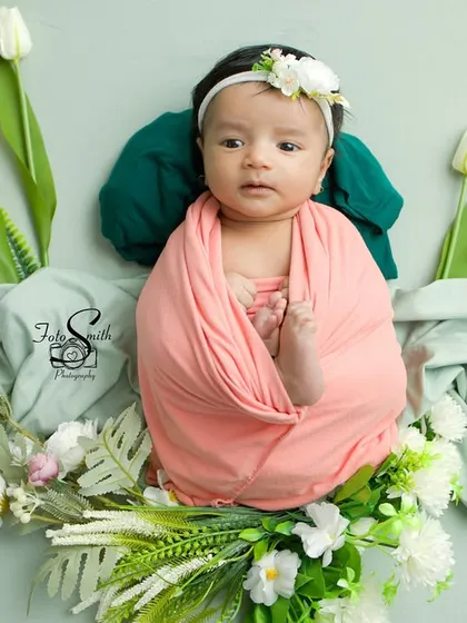 A top-down view of a baby swaddled in pink, framed by white tulips. This angle creates a beautiful, symmetrical composition.