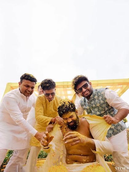 The groom's friends playfully showering him with turmeric and flowers during his Haldi ceremony.
