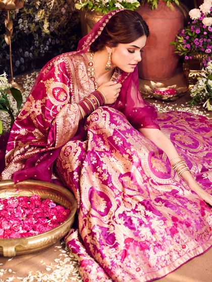 A beautiful composition of the bride in her traditional magenta attire, surrounded by flowers. This look is perfect for a bride or newlywed celebrating a special occasion.
