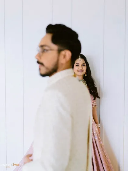 A creative portrait with the groom in the foreground, slightly out of focus, and the bride peeking out from behind him with a smile.