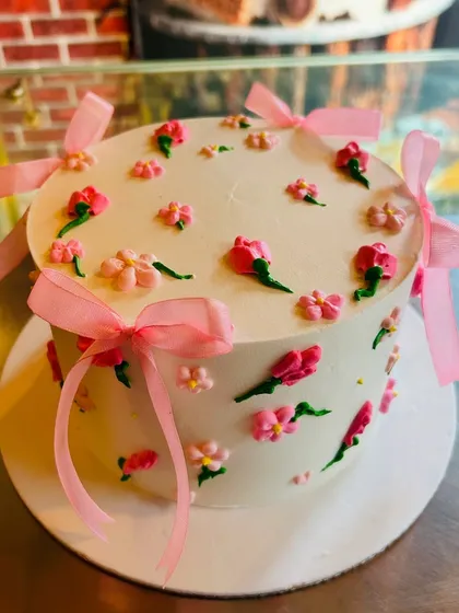 A delicate and pretty cake with tiny piped flowers and soft pink ribbons, giving it a lovely, gentle look.