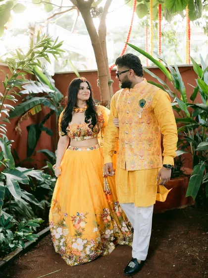 A couple walking hand-in-hand during their Haldi function, coordinated in beautiful floral yellow outfits.