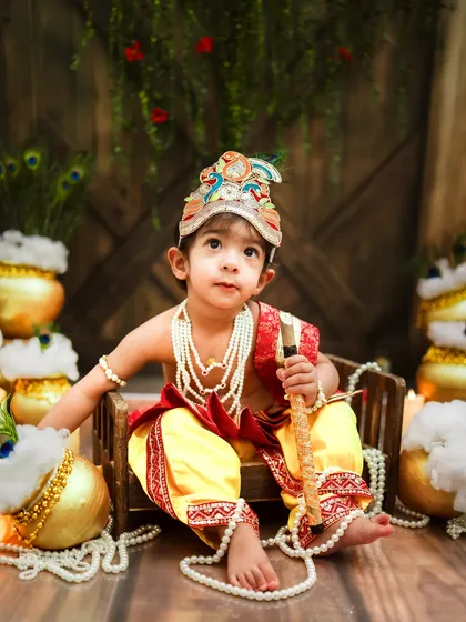 A thoughtful little Krishna, holding his flute. The warm lighting and rustic background create a timeless feel.