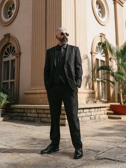 A groom in a sharp all-black suit stands confidently before a grand, classic building. This portrait is the epitome of timeless elegance and masculine grace.