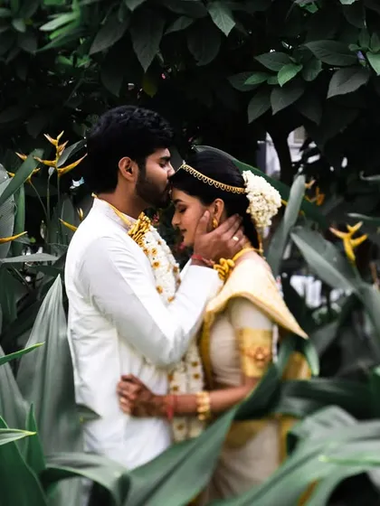 A tender forehead kiss, framed by lush green leaves. This is a classic, intimate shot that feels very private and romantic.