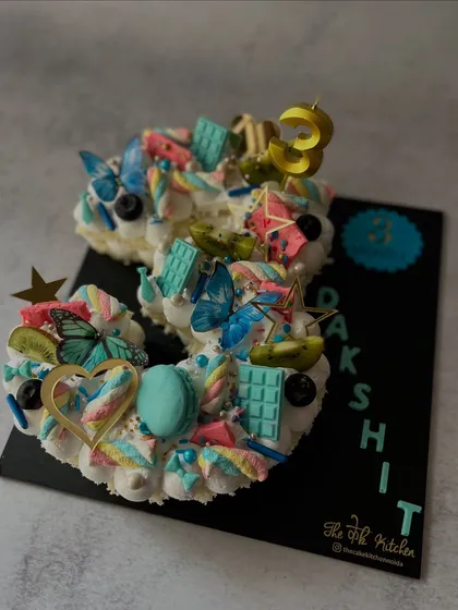 This number 3 cake has a whimsical, fairy-garden feel. It's decorated with pastel buttercream, edible butterflies, macarons, marshmallows, and fresh kiwi slices for a light and colorful celebration cake.