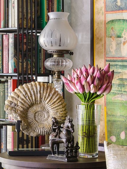 A sofa-end table in the Courtyard Home holds an eclectic mélange of objects: a 19th-century crystal Osler lamp, a large fossilized ammonite, and an 18th-century bronze of Shiva. This composition reflects a deep love for history, nature, and art.