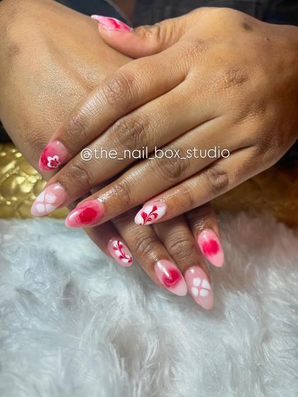 A beautiful set of acrylic extensions with intricate art. The design features a blend of red and pink with white floral and lattice patterns, creating a very romantic and detailed look.