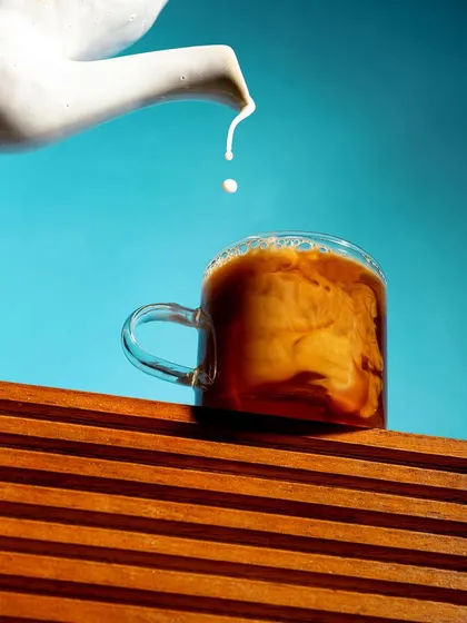A creative and minimalist shot of a single drop of milk falling into a cup of coffee. The stark contrast between the bright blue background and the warm wood creates a visually striking and artistic image.
