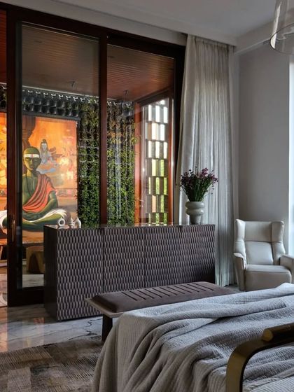 This bedroom in the 'Vrinda' project is a serene retreat. A large painting of Buddha is visible through a glass partition, connecting the room to a tranquil outdoor space and infusing it with a sense of spirituality.