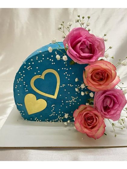 A beautiful blue top forward cake decorated with fresh roses and golden hearts. This style offers a unique canvas for floral arrangements.