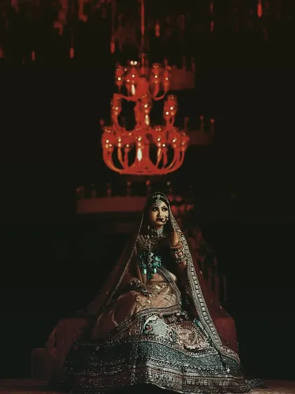 A moody and dramatic bridal portrait, with the bride seated under a grand chandelier, creating a very cinematic feel.
