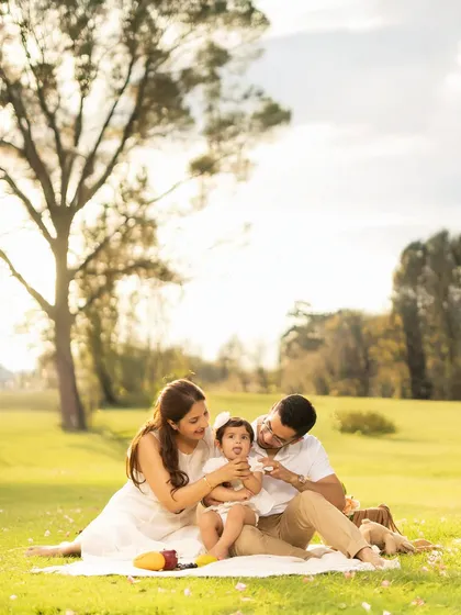 A family shares a tender moment during a picnic, with the parents focused lovingly on their baby. The golden hour lighting and natural park setting create a warm and intimate atmosphere.
