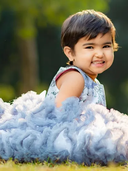A lovely outdoor portrait of little Aradhya, whose cheerful smile lights up the frame. Her beautiful ruffled dress adds a touch of elegance to this natural light kids photoshoot.