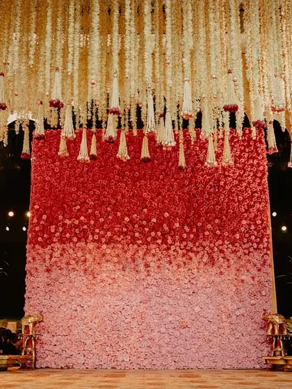 The full floral wall is visible here, a breathtaking canvas of color and texture that serves as the centerpiece of the mandap design.