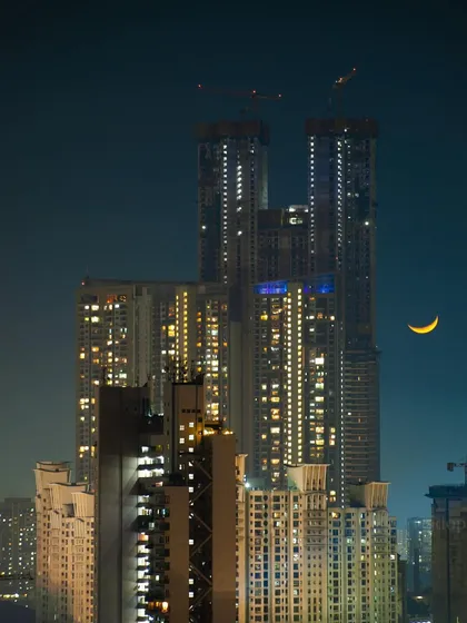 A crescent moon shines in the night sky next to the towering, under-construction Palais Royale in Mumbai.
