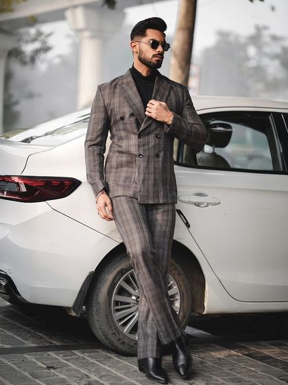 An outdoor shot from a men's fashion editorial, featuring a model in a plaid suit leaning against a white car. This style of automotive and fashion photography creates an aspirational, high-end lifestyle image for the brand.