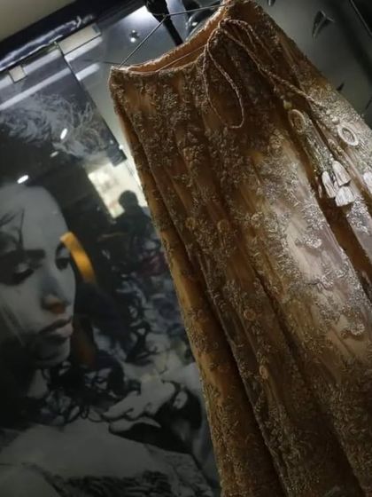 A creative shot of the bridal lehenga on display. The reflection of a portrait in the glass adds a layer of depth and artistry to what would be a simple detail shot.