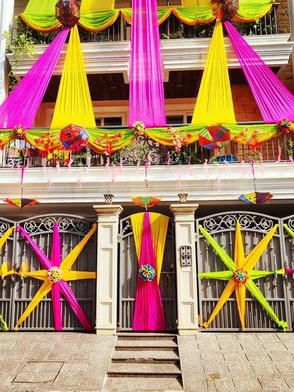 A stunning home exterior featuring multi-level draping in bright yellow and pink, with decorative stars on the gate to match.