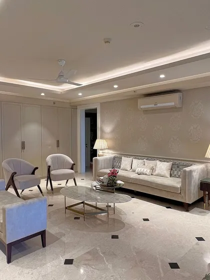 In this living room, we used a subtle stencil pattern on the wall to add a layer of bespoke elegance. The classic furniture shapes, neutral tones, and marble flooring with black inlays create a timeless and sophisticated look.