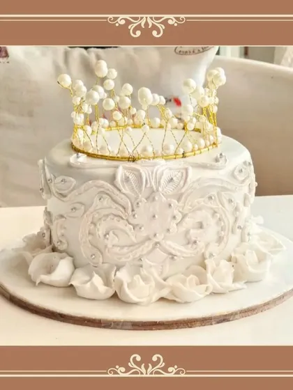 A regal white cake with intricate detailing and a stunning handmade pearl and gold crown.