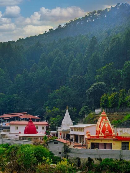 The Kainchi Dham temple complex set against a backdrop of dense green forests in Uttarakhand. This photo captures the spiritual tranquility and beautiful natural surroundings of the famous ashram.