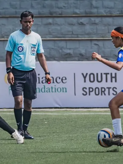 An action shot from the Reliance Foundation Young Champs Football Cup, with our player skillfully dribbling past a defender under the watchful eye of the referee.