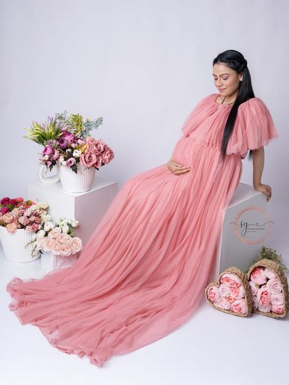 A graceful seated portrait of the mom-to-be. The long train of the pink tulle gown and the floral props create a soft and romantic setting.