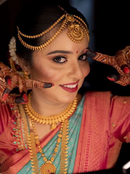 A playful and happy bride framing her face with her henna-adorned hands. Her traditional jewelry and saree complete the stunning bridal look.