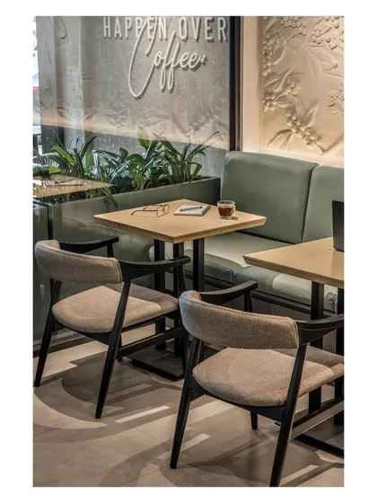 The seating arrangement combines soft textures, earthy tones, and a thoughtful layout to ensure the setting is as inviting as the coffee it serves. The brand's tagline is visible on the glass, reinforcing the atmosphere.