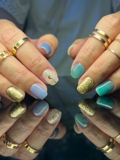 A cool and trendy mix of pastel blue, teal, and gold glitter nails, with a delicate moon accent.