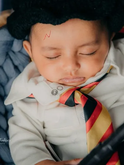 A close-up of baby Harry, complete with the iconic scar and Gryffindor scarf. He's sleeping soundly, probably dreaming of Hogwarts.