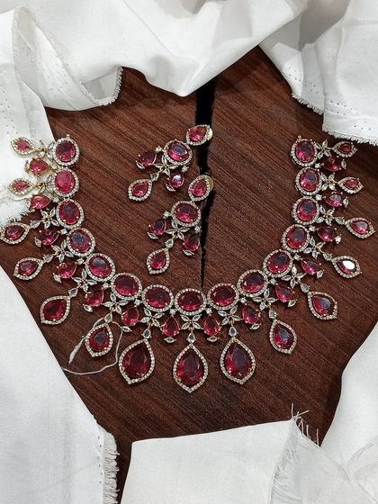A stunning AD necklace set with ruby-red stones, laid out to showcase its intricate, flowing design.