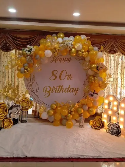We specialize in elegant decorations for major milestones, like this beautiful 80th birthday setup. The design uses a sophisticated gold and white color scheme with a custom round backdrop, marquee numbers, and decorative paper flowers.